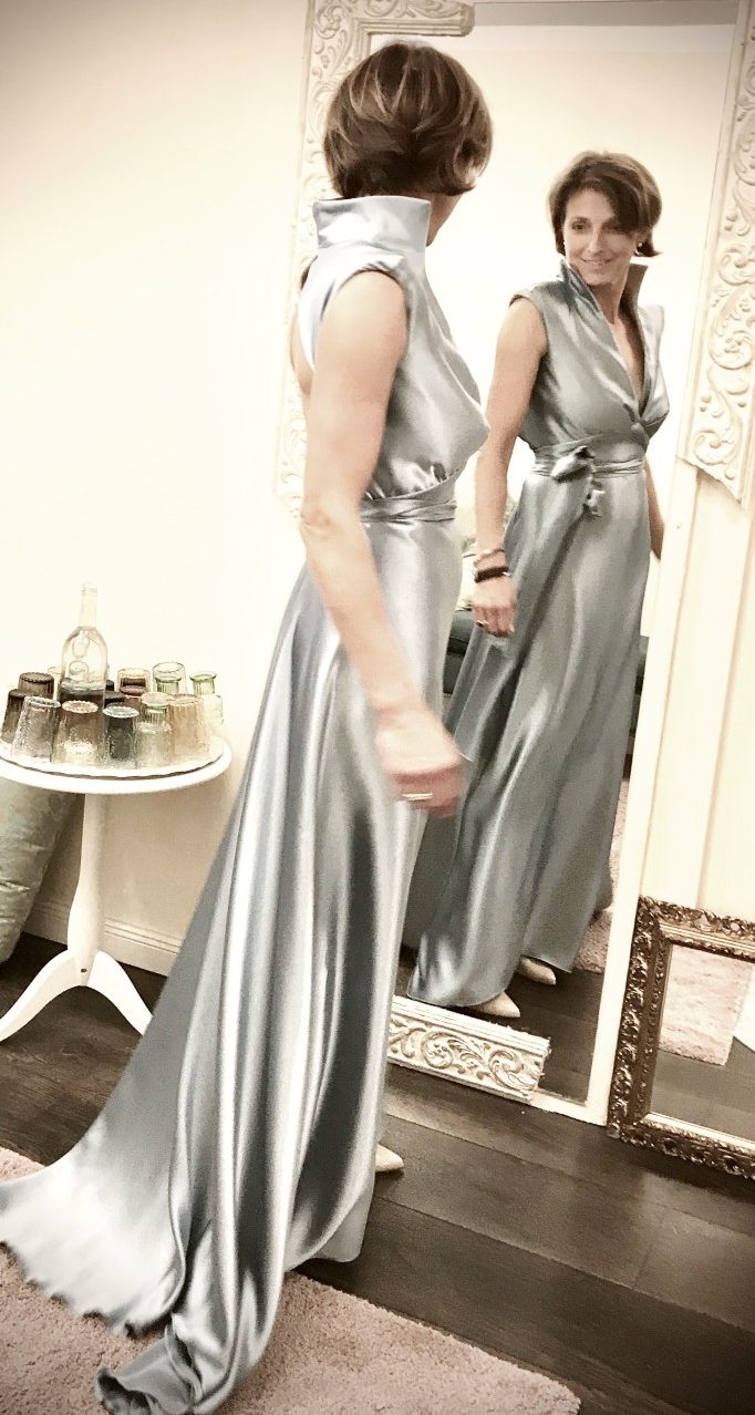 Frau vor Spiegel und dreht sich im eleganten Satin Abendkleid mit Schulterpolstern